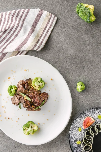 Top view of broccoli and fried meat on white plate and fig with onion on black plate — Stock Photo