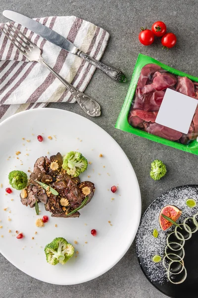 Vista dall'alto di broccoli e carne fritta su piatto bianco e fico con cipolla su piatto nero con carne cruda sul tavolo — Foto stock