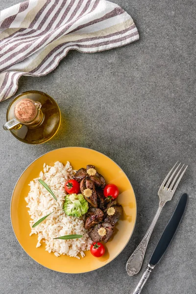 Vista superior del arroz, la carne y el brócoli en el plato con aceite, tenedor y cuchillo - foto de stock