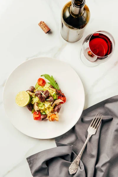 Top view of salad on white plate with glass and bottle of wine — Stock Photo
