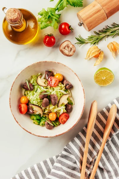 Top view of salad on white bowl with bottle of oil, cherry tomatoes, lime and rosemary — Stock Photo