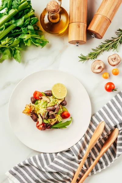 Salade sur assiette blanche avec bouteille d'huile, tomates cerises, citron vert et romarin — Photo de stock