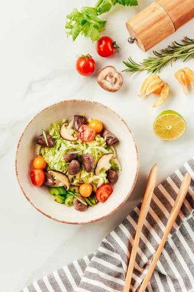 Insalata su ciotola bianca con bottiglia di olio, pomodorini, lime e rosmarino in tavola — Foto stock