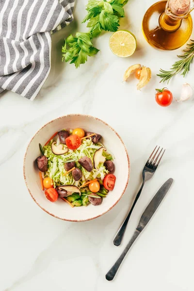 Salad on white bowl with bottle of oil, cherry tomatoes, lime and rosemary on table — Stock Photo