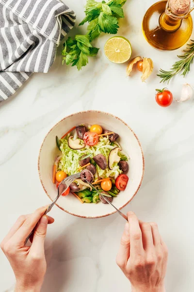 Vista ritagliata di donna che mangia insalata con forchetta e coltello — Foto stock