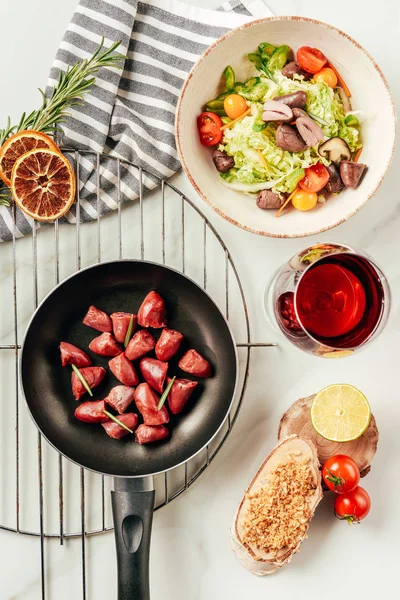 Top view of meat in frying pan and salad with glass of wine — Stock Photo