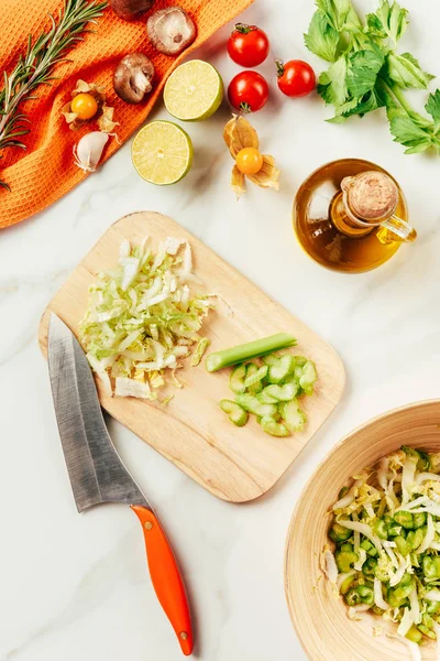 Cabbage and celery on cutting board with bottle of oil, cherry tomatoes, limes and rosemary — Stock Photo
