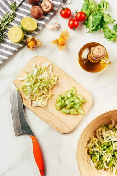 Top view of cabbage and celery on cutting board with bottle of oil, cherry tomatoes, limes and rosemary — Stock Photo