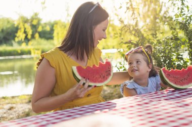 Anne ve kızı piknikte karpuz dilimi yiyor