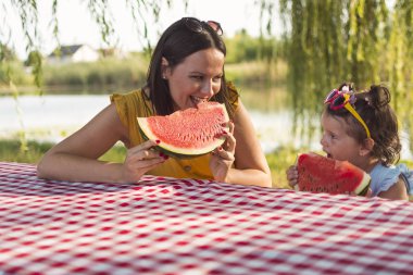 Anne ve kızı piknikte karpuz dilimi yiyor