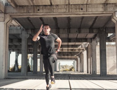 Bir sporcu rustik, bitmemiş binada sprint eğitimi vardır. Hareket halindeki koşucunun düşük görüş açısı, zıplamomenti. Beton, gri ortam.