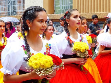 Cuenca, Ekvador - 11 Nisan 2019: Cuenca şehrinin kurulduğu gün geleneksel geçit töreni veya desfile. Güzel genç kadın halk dansçıları il Azuay (cuencana) tipik kostümleri çiçek hem il bayrağı renklerinde yapılan - kırmızı ve bağırmak