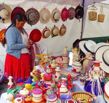 Cuenca, Ekvador-8 Mart 2019: Kadın, toquilla saman veya sebze lifi ile yapılan ve esnaf pazarında çeşitli renklerle boyanmış hediyelik eşya (sepet, bebek, şişe, vazo, ) yapar ve satıyor, Cuenca