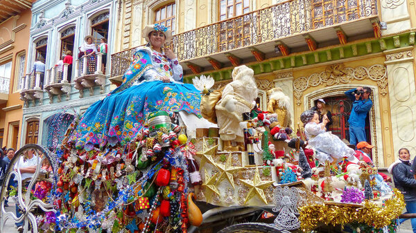 Cuenca, Ecuador - December 24, 2018: Christmas parade Pase del Nino Viajero. Woman dressed up for parade in rich colorful traditional costume with embroidery rides a coach with christmas decoration