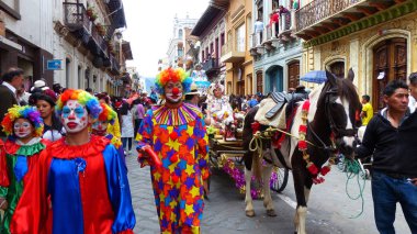 Cuenca, Ekvador - 24 Aralık 2018: Noel geçit töreni Pase del Nino Viajero. Renkli kostümlü palyaçolar ve nakışlı geleneksel kostümlü kadın noel dekorasyonu ile bir koça biniyor