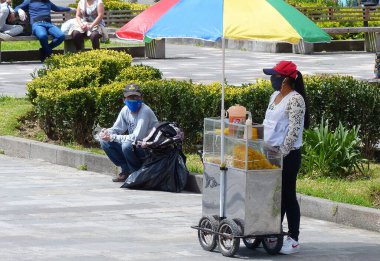 Cuenca, Ekvador - 27 Mayıs 2020: Plaza Civica, Cuenca 'nın tarihi merkezindeki 9. Maskeli kadın COVID-19 sırasında meyve suyu, patates cipsi, patlamış mısır, fındık satıyor.