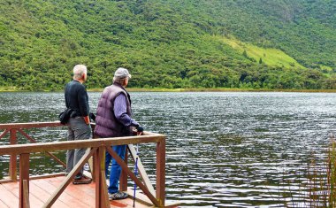 Azuay ili, Ekvador - 16 Mart 2020: Cajas Milli Parkı, Llaviuco Gölü. Balıkçı güvertesinde iki kıdemli turist dağ doğasıyla eğleniyor. Ekvador