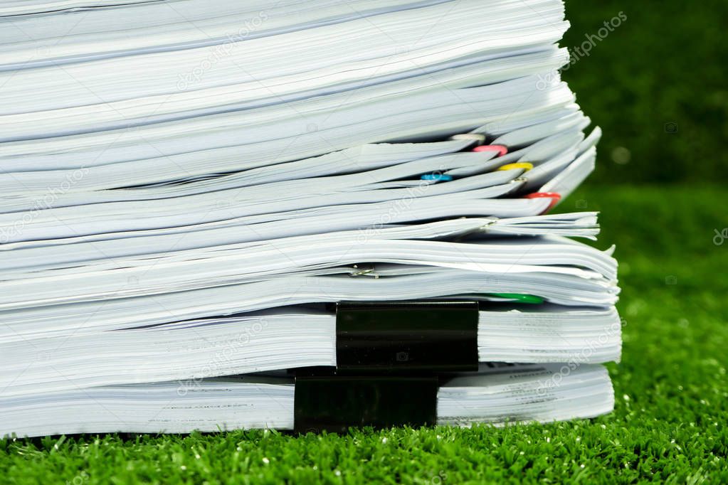 Documents pile on grass in concept save Earth and use paper economically and cost-effectively.