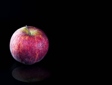 Siyah arka plan üzerine parlak yüzeyi su damlacığı ile kırmızı elma.