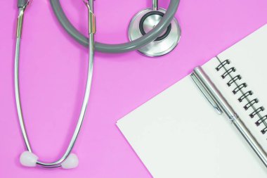 Stetoskop ile boş defter ve kalem pembe bir arka plan üzerinde.