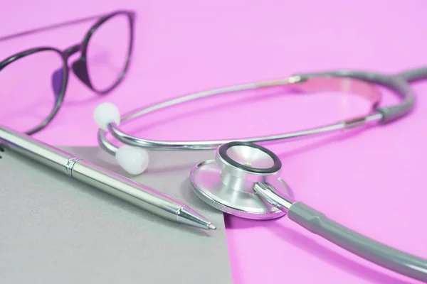 空白のノートブックにメガネとピンクの背景のペンの聴診器 — ストック写真