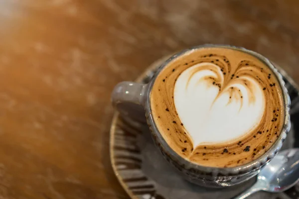 Hot coffee with heart-shaped froth on wooden table.