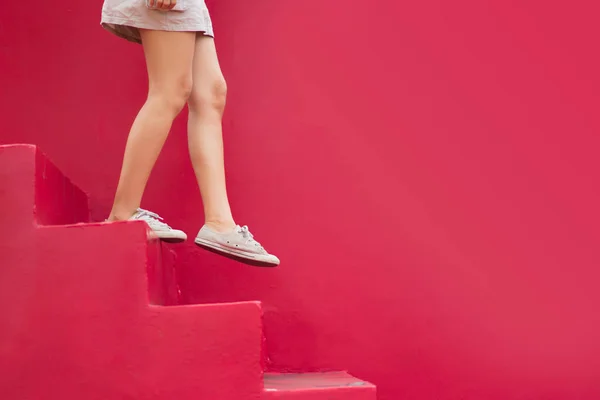 Legs of woman walking down red stair with copy space on red background.