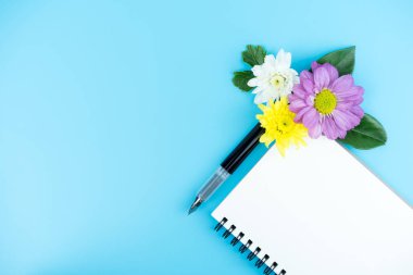 Blank notebook with Ink pen and decorate flowers and green leaf on color background