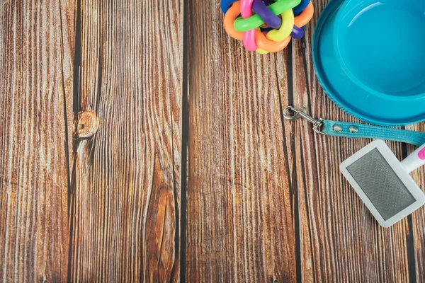 Pet accessories concept.  Pet bowl with rubber toy and leashes on wooden background.