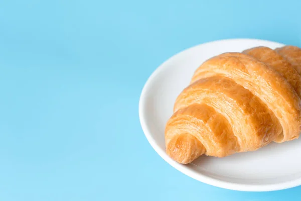 Croissant in einem weißen Teller auf farbigem Hintergrund — Stockfoto