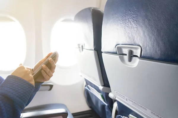 Hand using smartphone and window in airplane with seats
