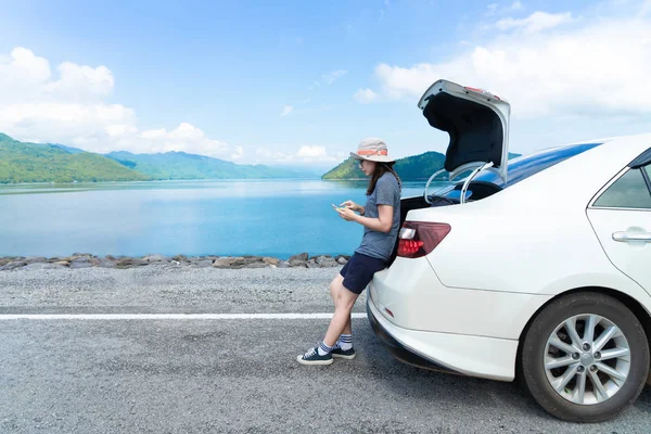 Woman traveler sitting on hatchback car and using smartphone — Stock Photo, Image