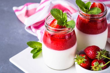 Panna cotta with strawberry jam. Sweet dessert from whipped cream with strawberry jam and fresh strawberies in glass jars. clipart