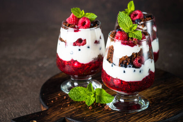 Layered dessert with sour cream, chocolate bisquit, jam and fresh berries in glass jar.