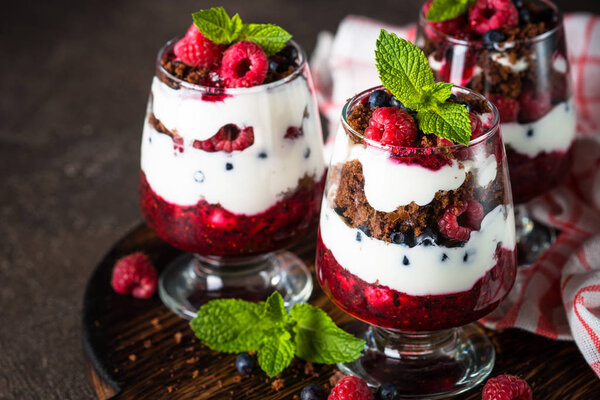 Layered dessert with sour cream, chocolate bisquit, jam and fresh berries in glass jar.