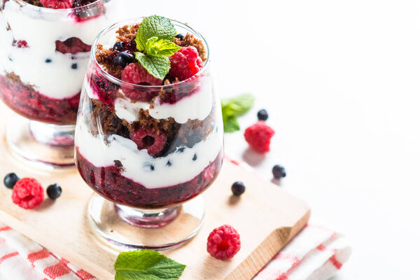 Layered dessert with sour cream, chocolate bisquit, jam and fresh berries in glass jar.