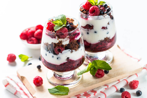 Layered dessert with sour cream, chocolate bisquit, jam and fresh berries in glass jar.
