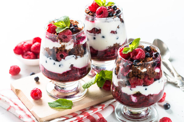 Layered dessert with sour cream, chocolate bisquit, jam and fresh berries in glass jar.