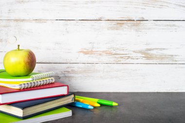 Kitap, defter, kalem ve elma yığını.
