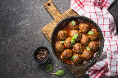 Karanlık taş masada bir tavada domates soslu köfte. 