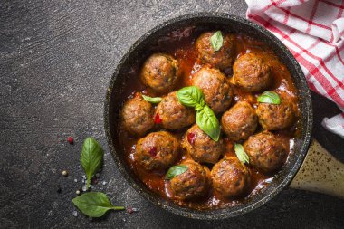 Karanlık taş masada bir tavada domates soslu köfte. 