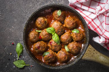 Karanlık taş masada bir tavada domates soslu köfte. 