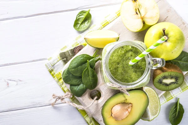 Green smoothie and ingredients on white wooden table. — Stock Photo, Image