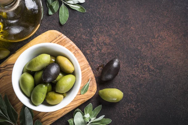 Black and green olives in a bowl and olive oil bottle on dark stone table. Top view with copy space.