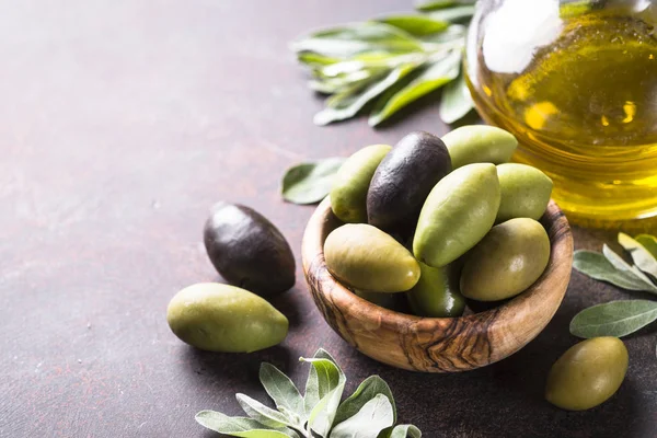 Siyah ve yeşil zeytin karanlık taş masada bir kase ve zeytinyağı şişede. Yakın çekim.