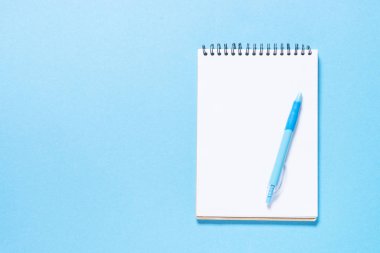 Defter ve kalem mavi zemin üzerine. Kopya alanı ile üstten görünüm.