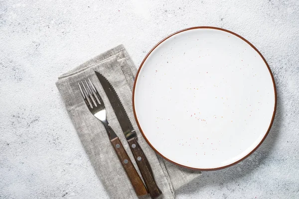 Beyaz tabak ve çatal bıçak takımı taş masa üstü görünümü. 