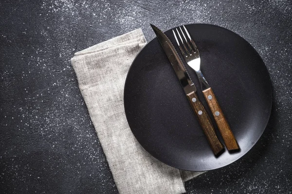 Siyah tabak, çatal bıçak ve peçete..