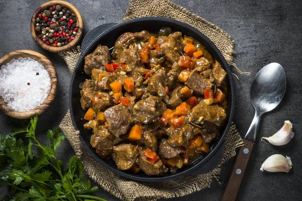 Estofado de ternera con verduras en sartén de hierro sobre negro . — Foto de Stock