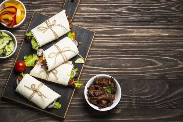 Burritos envolturas de tortilla con carne de res y verduras en respaldo de madera —  Fotos de Stock